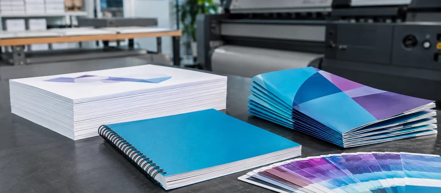 Printed brochures, bound documents and cyan color samples on a print-work table.